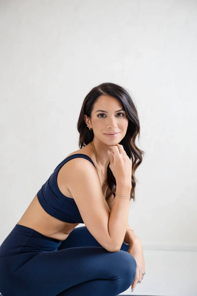 Woman in navy athletic set posing against a pale gray wall chin resting on her hand