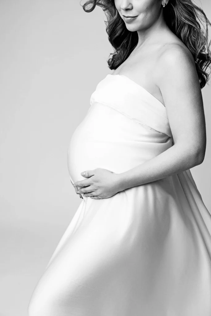 Side profile of a pregnant woman in a strapless dress cradling her baby bump